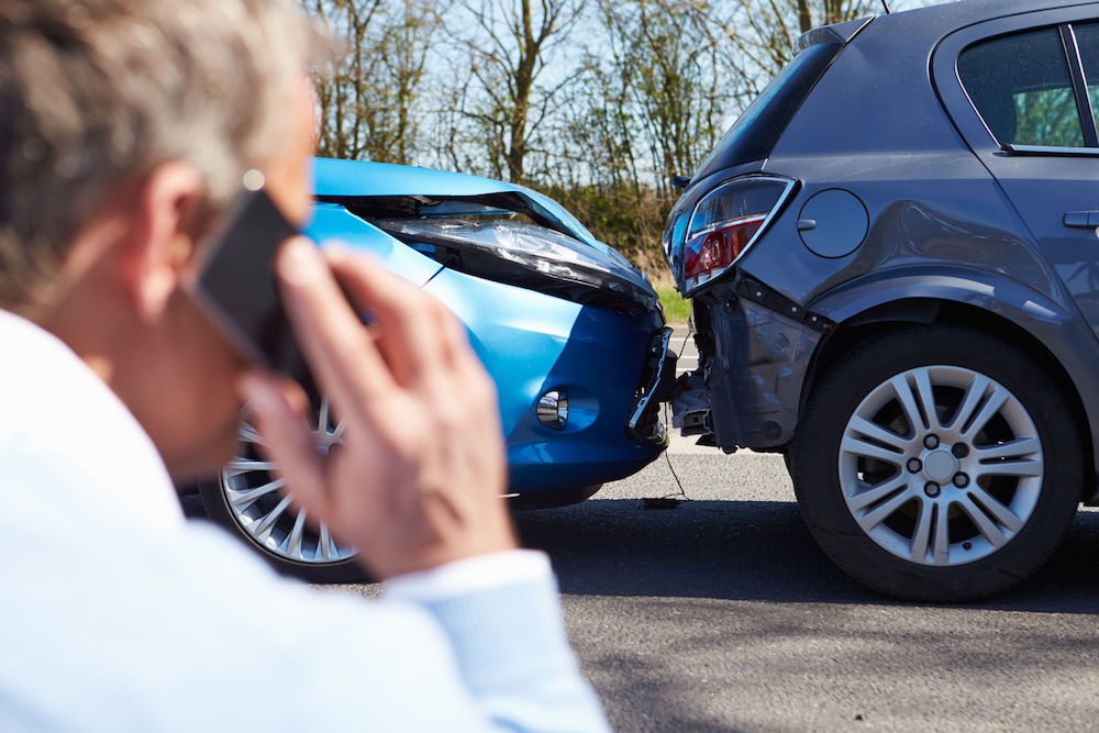 Man on Phone Looking at Car Accident Needing Auto Insurance in Bay City, Midland, Oscoda, Saginaw, and Tawas City