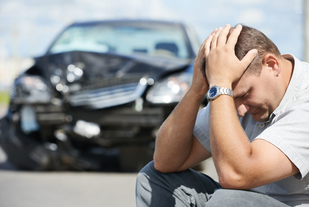 Man Sitting on Road by Beat Up Car with Hands on Head Needing Auto Insurance in Saginaw, MI